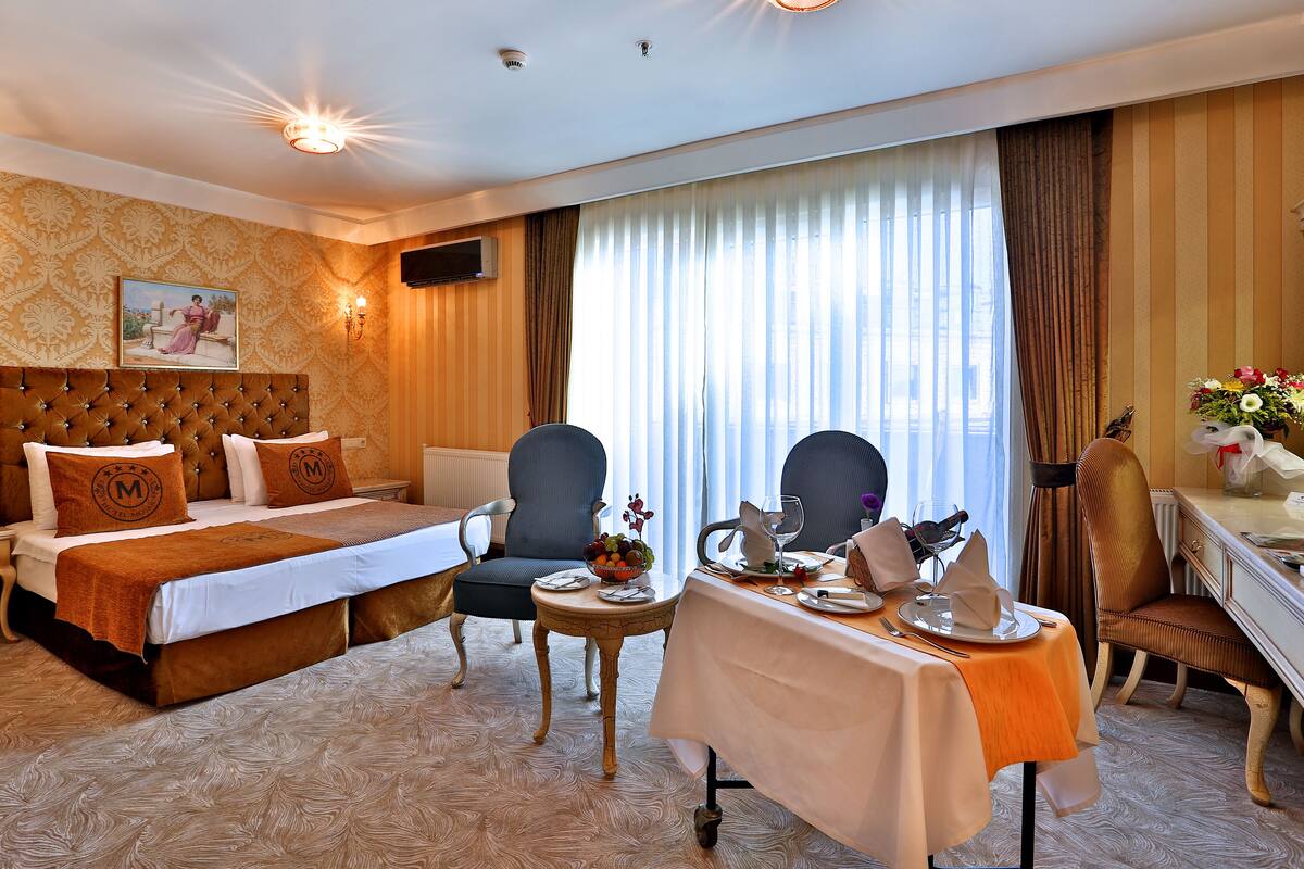 A hotel room with a large bed, two armchairs, a small table set for dining, and a desk with a chair.