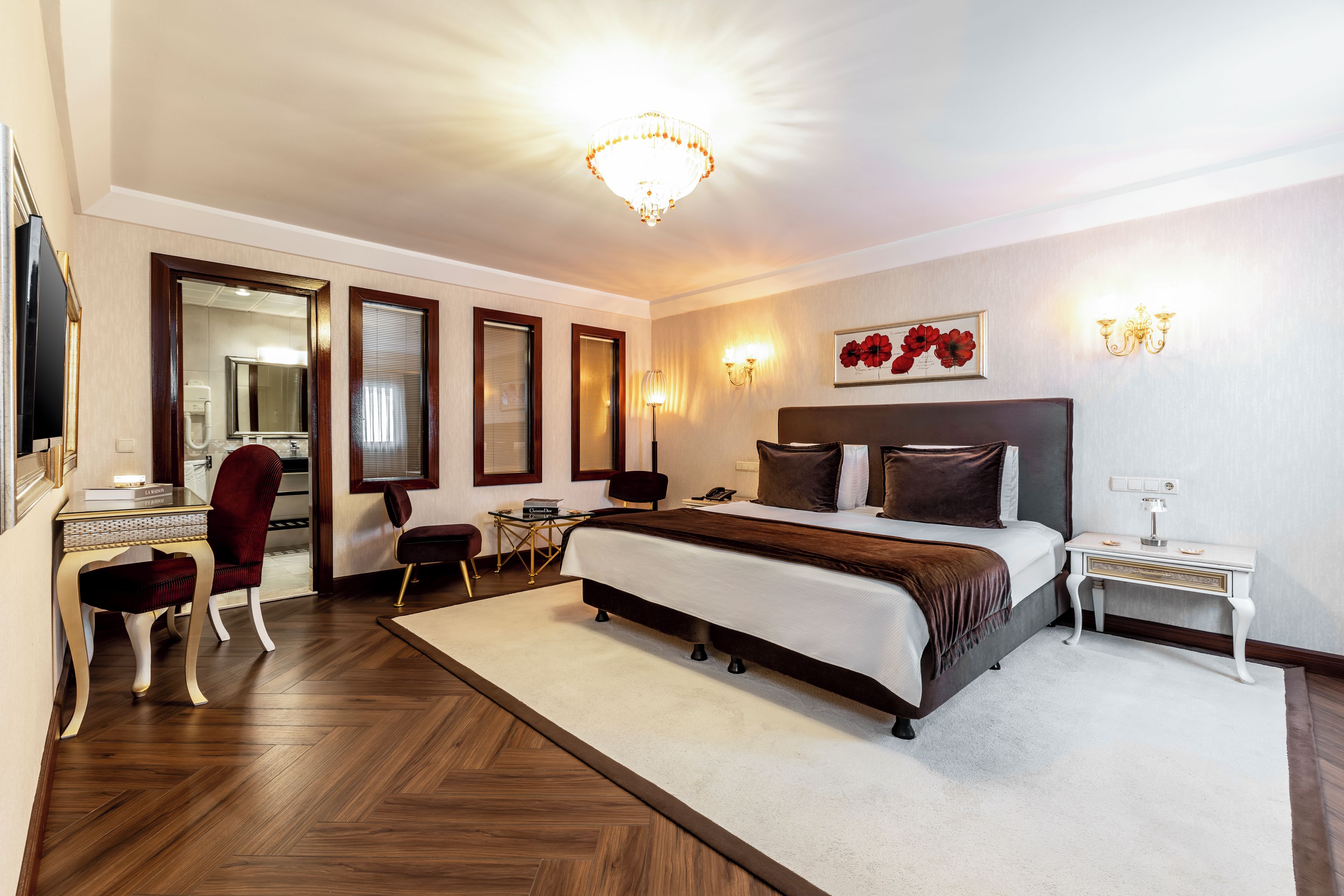 A hotel room with a large bed, a desk, a chair, a mirror, and a chandelier.