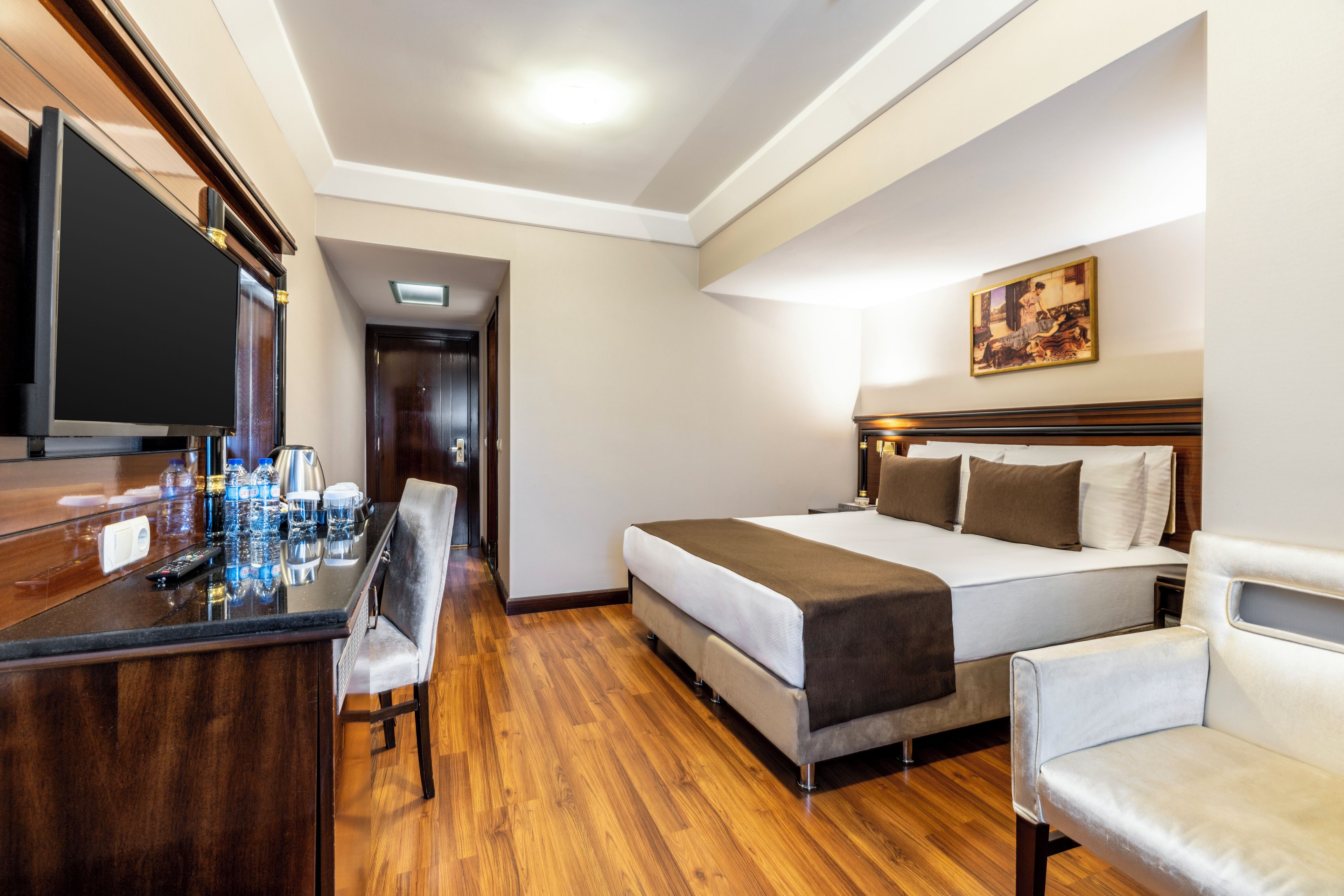 Una habitación de hotel con una cama, un escritorio con televisor y un cuadro en la pared.