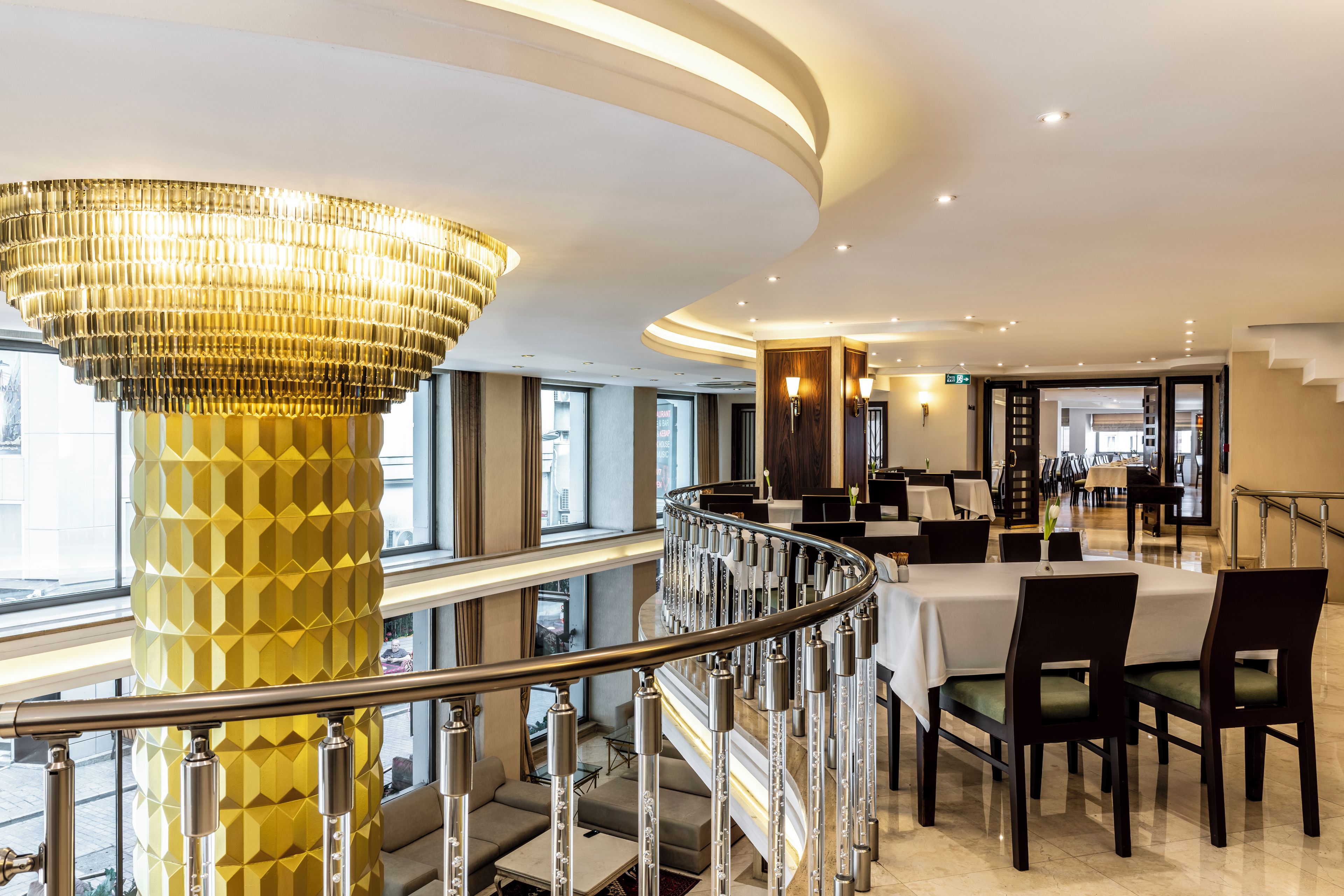 A hotel lobby with a modern chandelier, a staircase, and a dining area with tables and chairs.