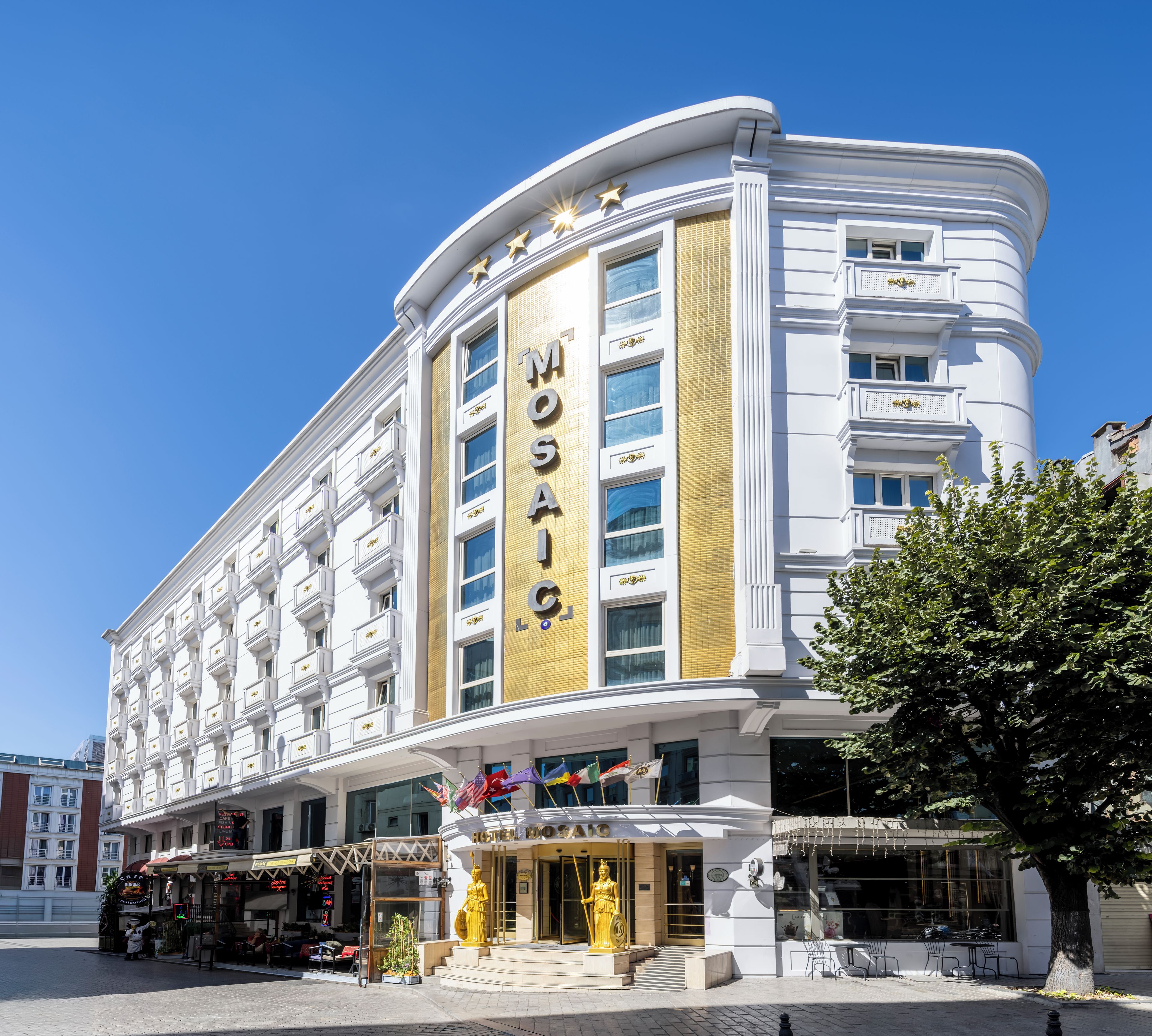 Un hotel con un llamativo letrero 'MOSAI', varios pisos y una estatua en la entrada.