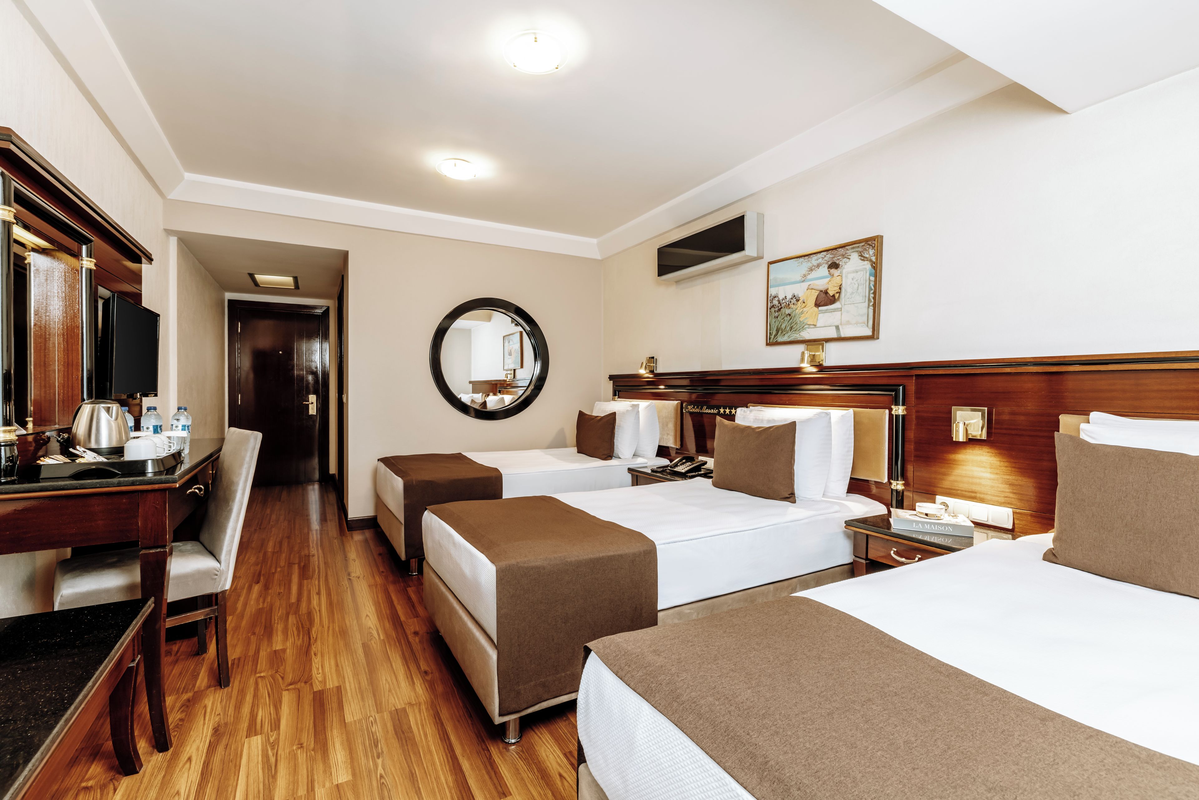 A hotel room with two beds, a desk, a mirror, and a painting on the wall.