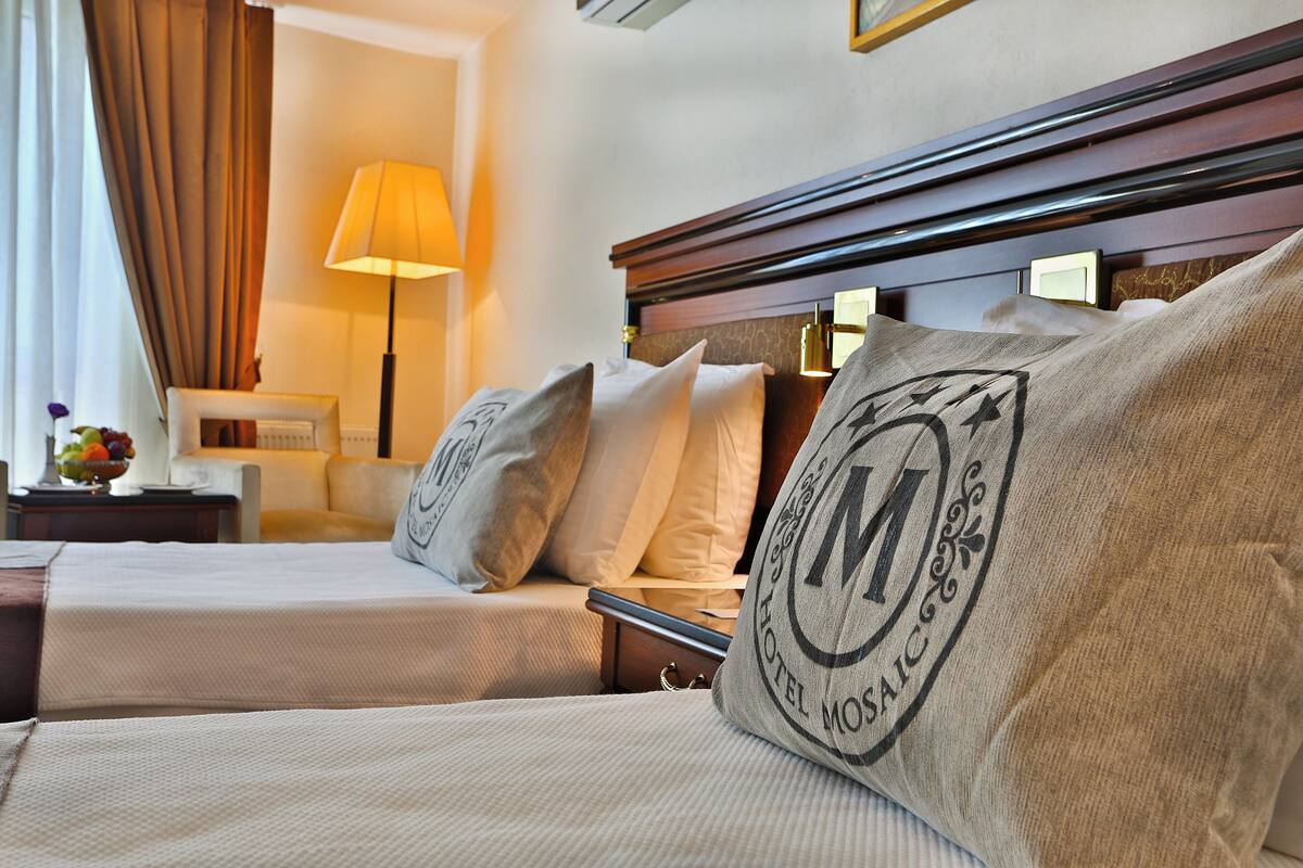 A hotel room with two beds, a nightstand, a lamp, and a view of the room.
