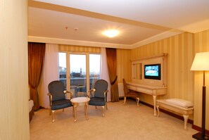A hotel room with two armchairs, a small round table, a television, a desk, and a lamp.