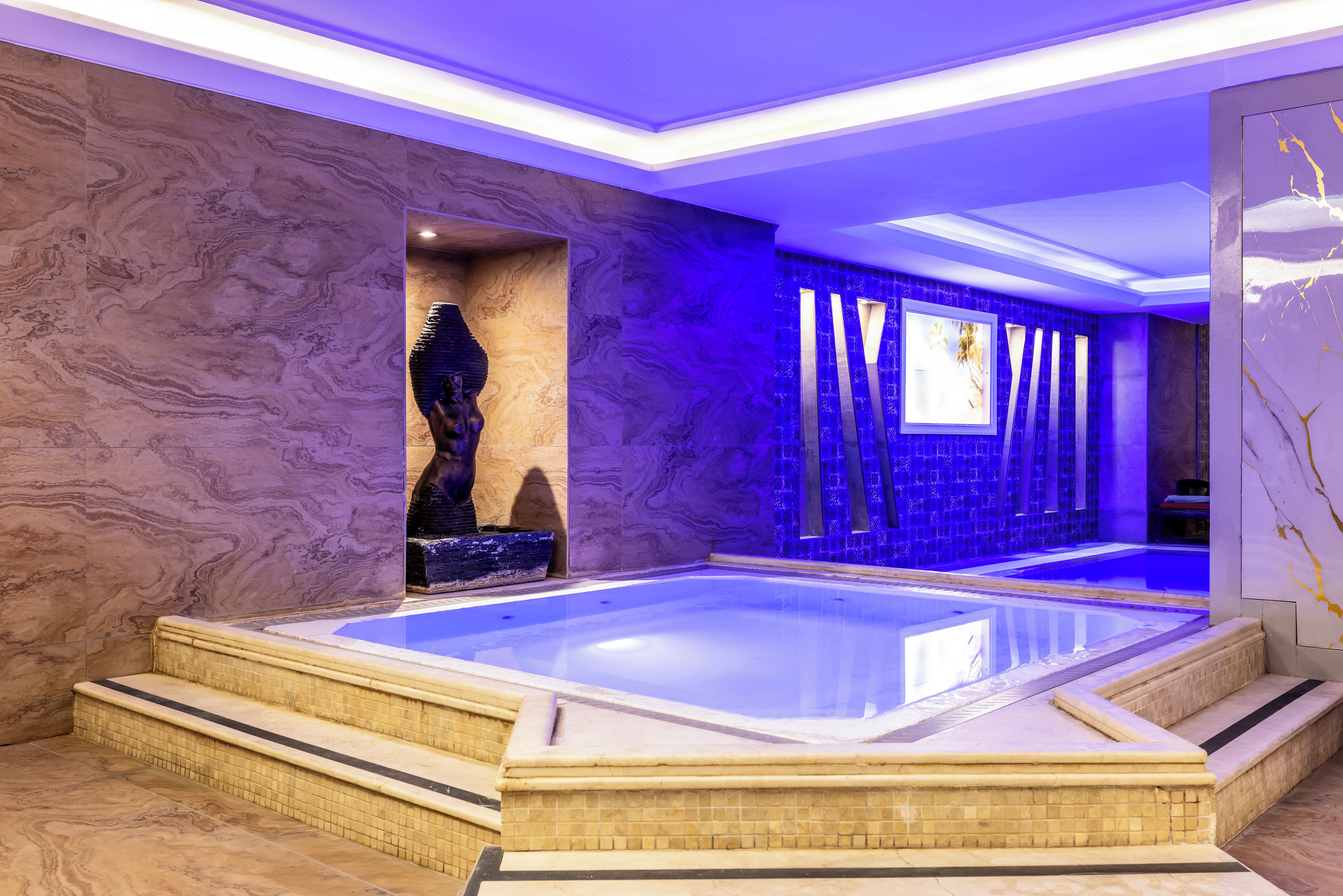 Un spa moderno con un amplio jacuzzi, paredes de mármol y una escultura decorativa.