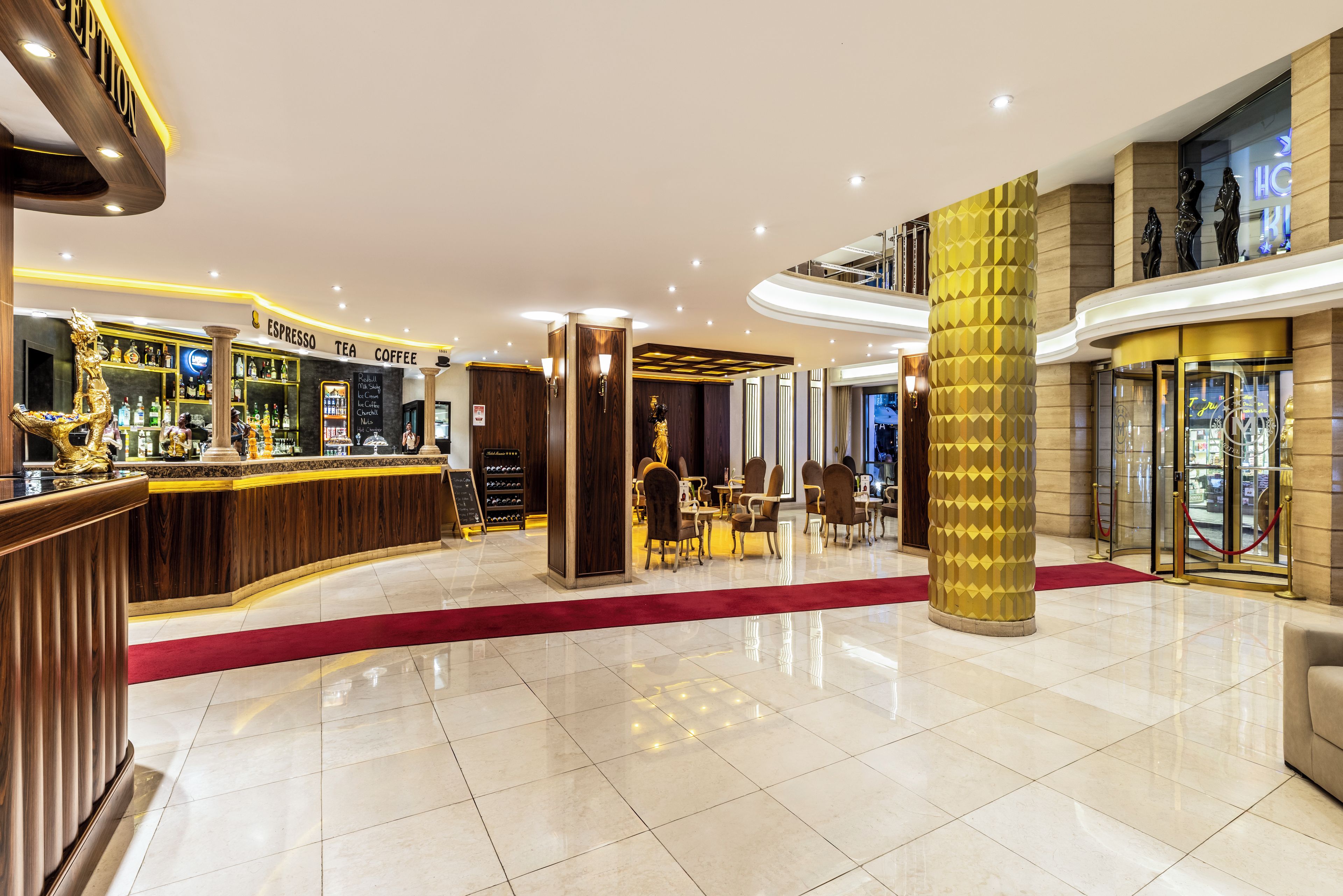 Un hall de hotel con mostrador de recepción, zona de bar y área de estar con mesas y sillas.