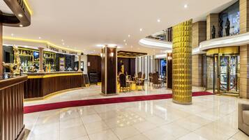 Un hall de hotel con mostrador de recepción, zona de bar y área de estar con mesas y sillas.