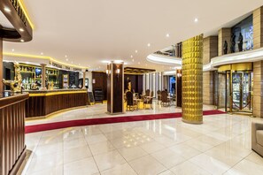 Un hall de hotel con mostrador de recepción, zona de bar y área de estar con mesas y sillas.