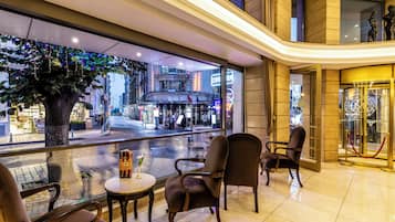 Un hall de hotel con vista a la calle, zona de estar y mostrador de recepción.