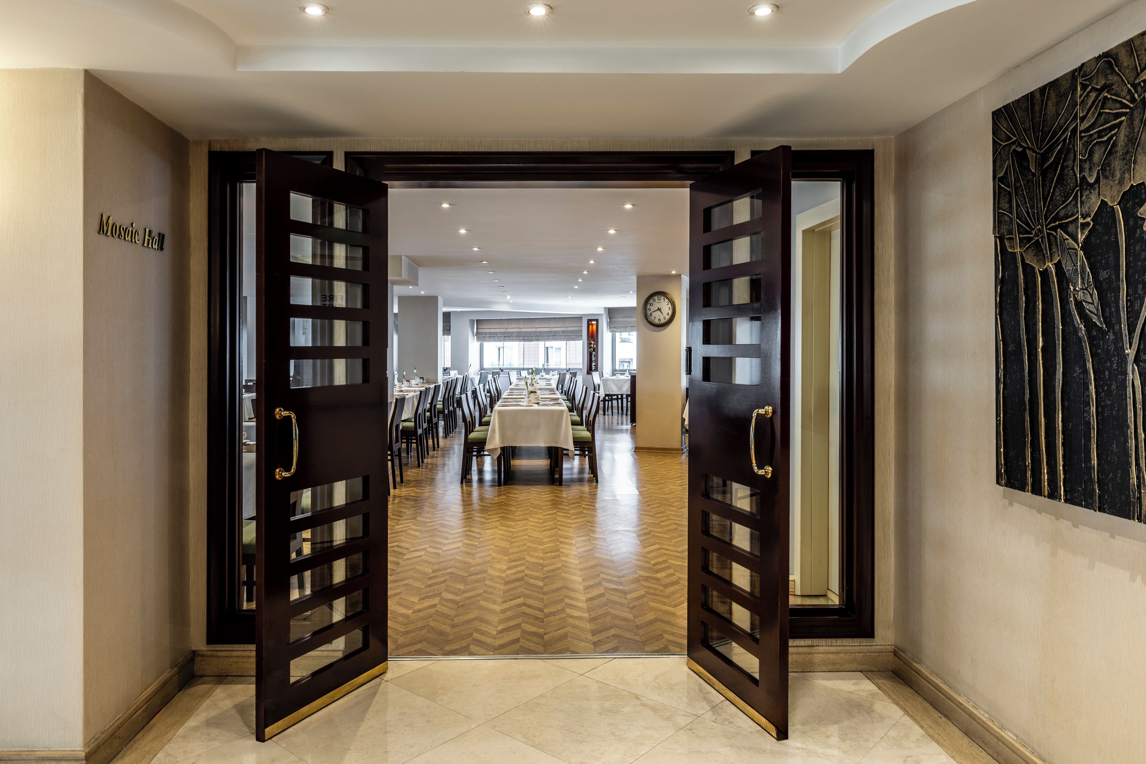 A hotel lobby with a long reception desk, a clock on the wall, and a large abstract art piece.
