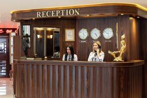 Un comptoir d’accueil avec un revêtement en bois, trois horloges indiquant différents fuseaux horaires et une statue dorée.