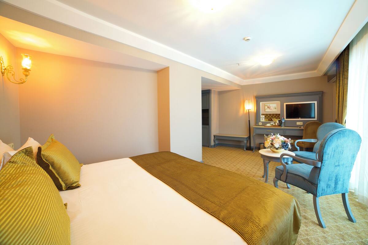 A hotel room with a large bed, a desk with a chair, a television, and a window with curtains.