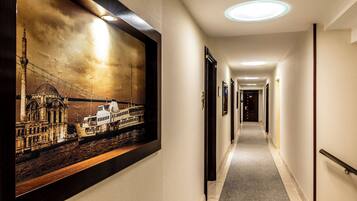 Pasillo de hotel con una fotografía histórica enmarcada en la pared, suelo alfombrado y una serie de puertas a lo largo del pasillo.