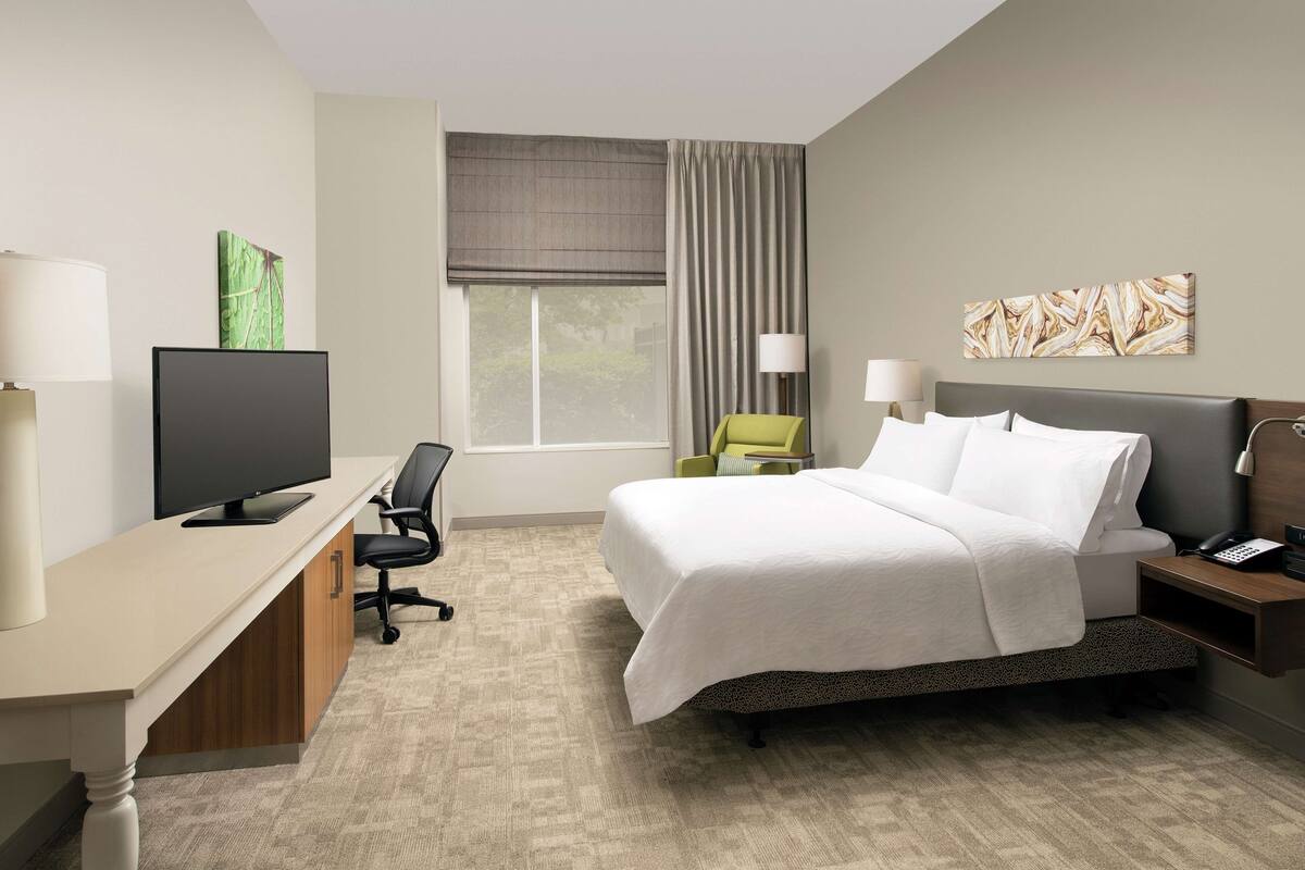 Une chambre d’hôtel avec un lit, un bureau, une télévision et une fenêtre avec des rideaux.