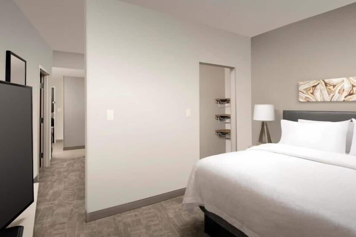 Une chambre d’hôtel équipée d’un lit, d’une télévision, d’un bureau et d’une porte donnant sur une autre pièce.