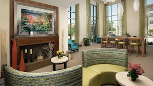 A modern lounge area with a fireplace, comfortable seating, a dining table, and large windows with curtains. - Hilton Garden Inn San Antonio Airport South (San Antonio)