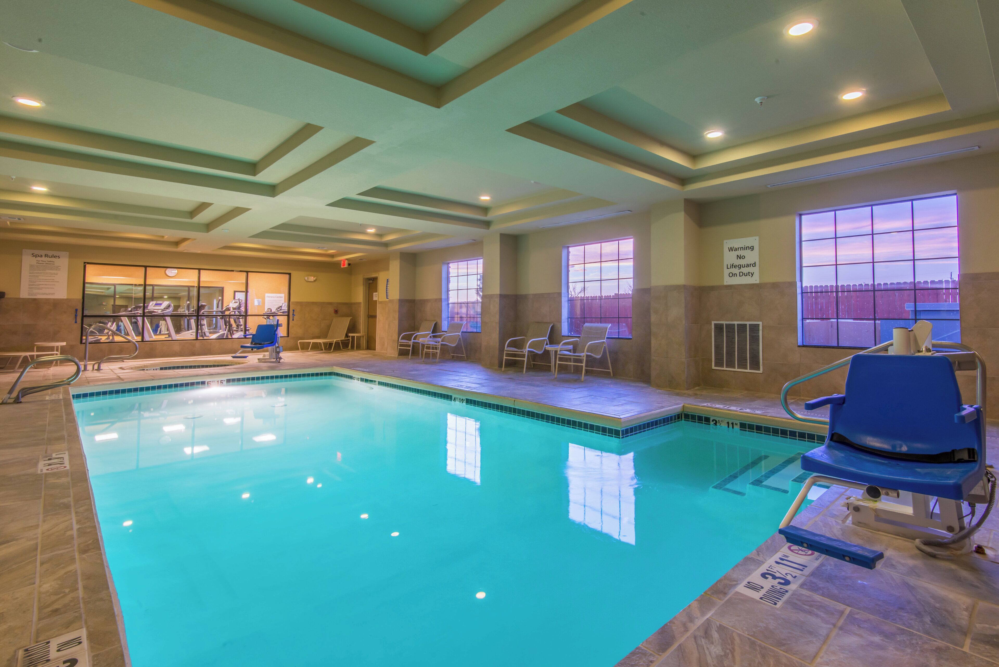 Une piscine intérieure à l’eau claire, entourée de chaises longues et d’un centre de remise en forme.