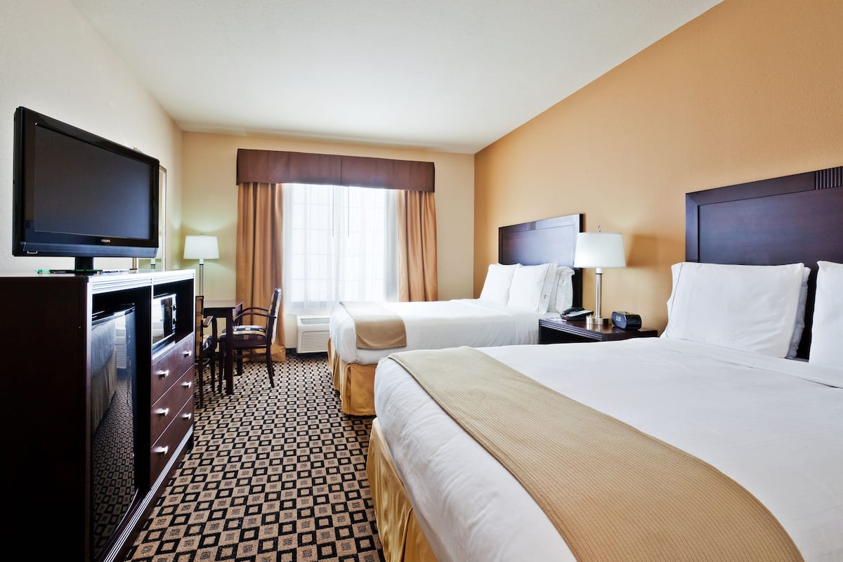 A hotel room with two beds, a television, a desk with a lamp, and a patterned floor.
