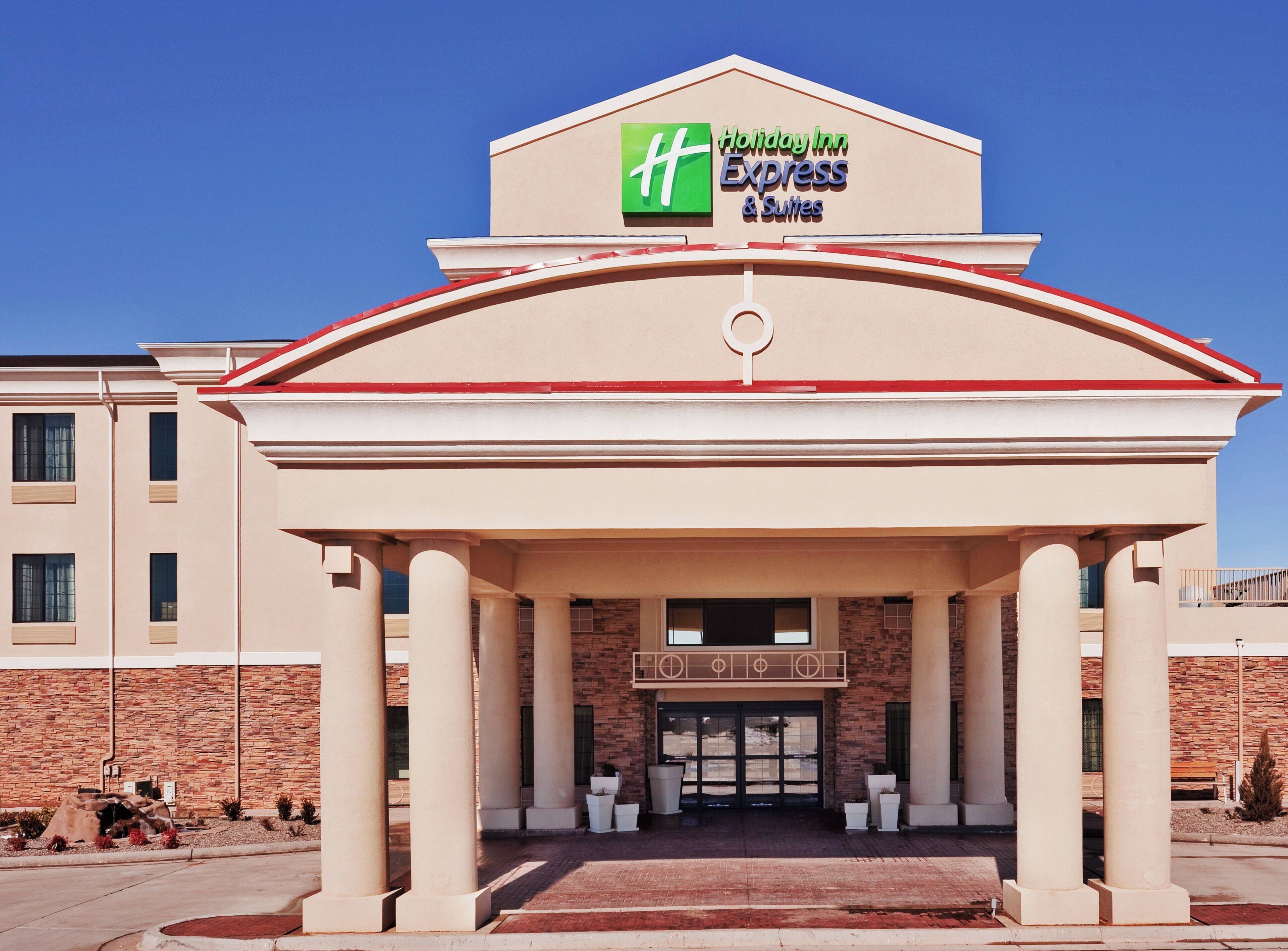 Un Holiday Inn Express & Suites con un llamativo logo H, fachada de ladrillo y una entrada simétrica con columnas.