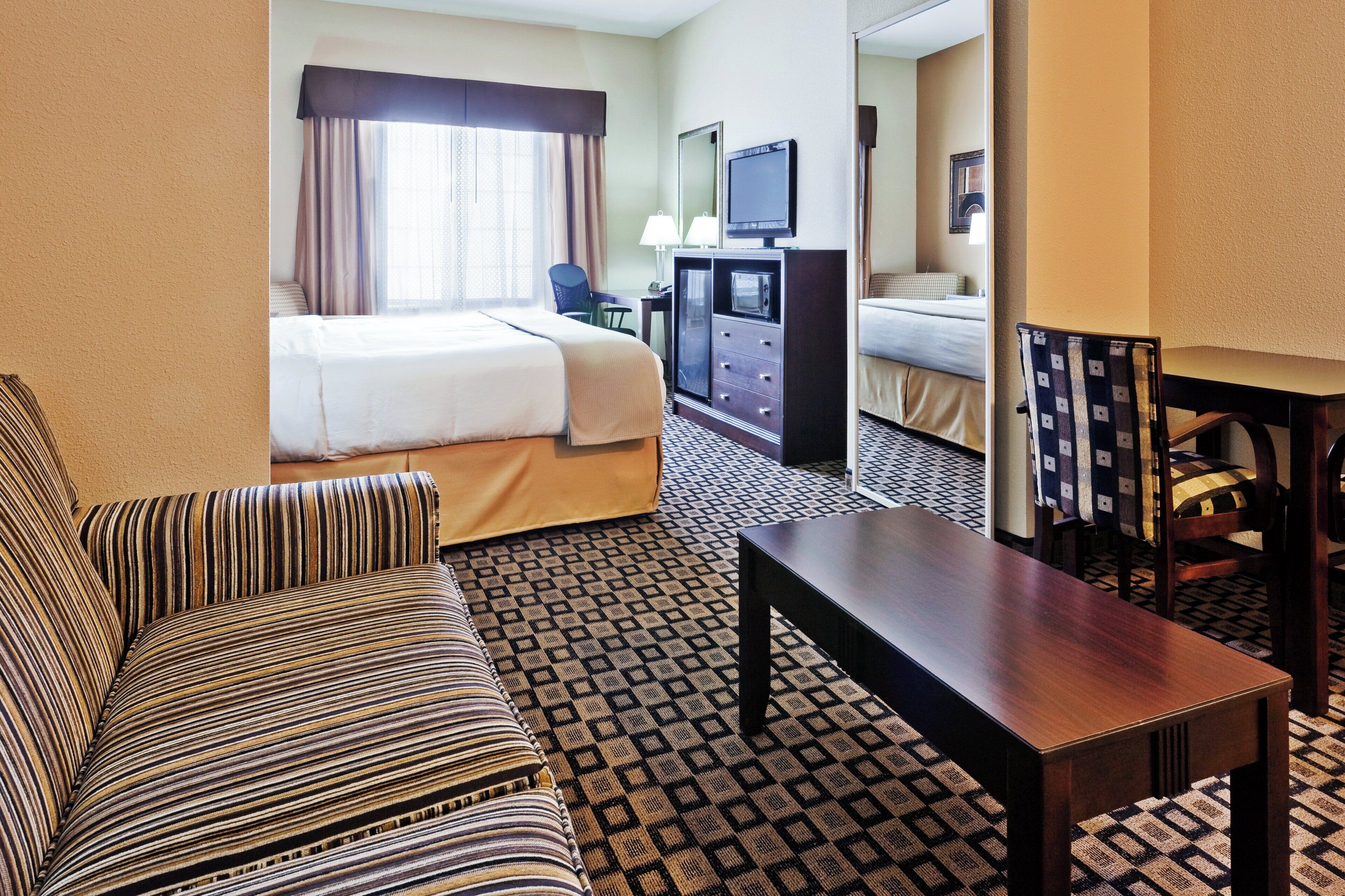 A hotel room with a bed, a sofa, a desk, a television, and a patterned floor.