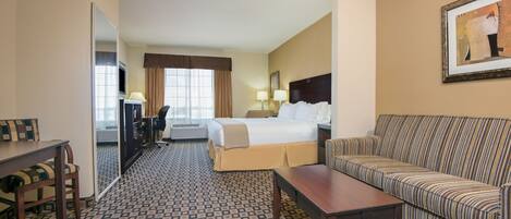 A hotel room with a bed, a sofa, a desk, a chair, and a patterned carpet.