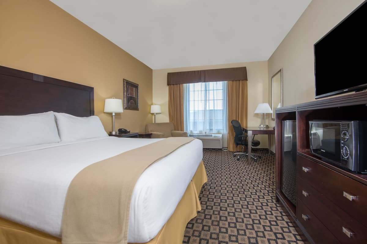 A hotel room with a large bed, a desk with a chair, a television, and a wardrobe.