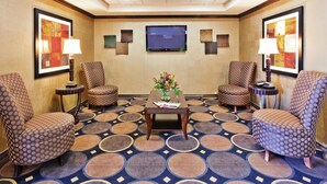 A hotel lobby with a patterned carpet, two armchairs, a coffee table, and a TV screen. - Holiday Inn Express Hotel & Suites Clovis by IHG (Clovis)
