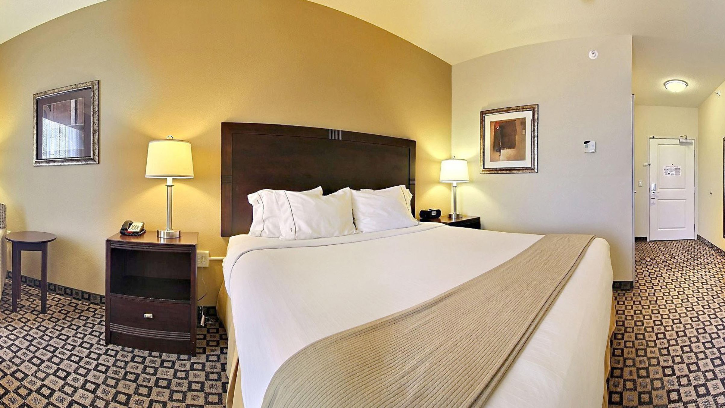 A hotel room with a large bed, two bedside tables with lamps, a small desk, and a chair.