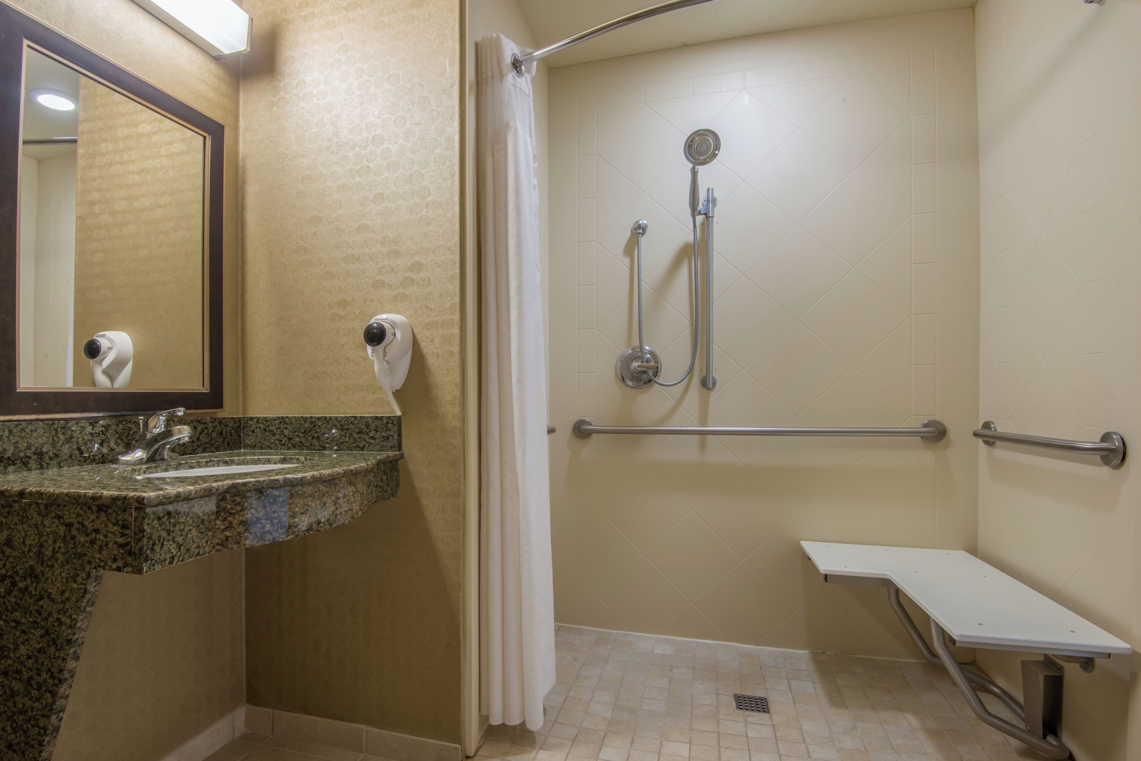 Une salle de bain équipée d’un lavabo en granit, d’une douchette à main, d’un sèche-cheveux portatif et d’une barre d’appui.