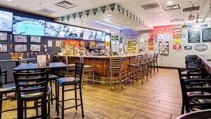 Una zona de bar con diferentes opciones de asientos, una barra con diversas botellas y recuerdos deportivos en las paredes.