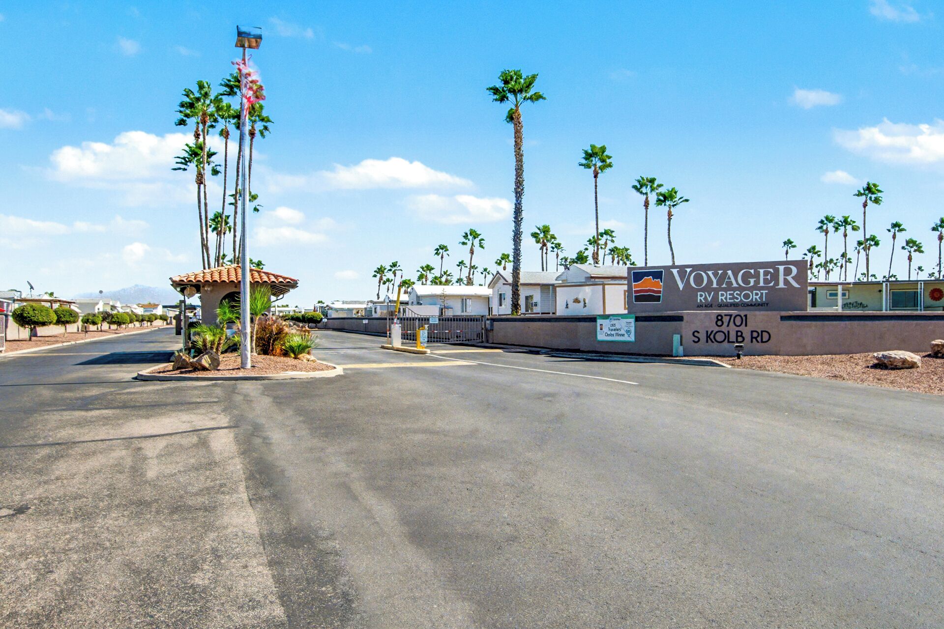 A sign for Voyager RV Resort with a clear sky and palm trees.
