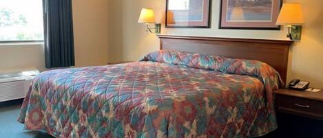 Quarto de hotel com uma cama grande, duas fotos emolduradas na parede, um abajur e um telefone na mesa de cabeceira.