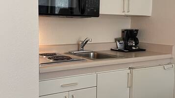 A compact kitchen with white cabinets, a black microwave, a coffee maker, and a stainless steel sink.