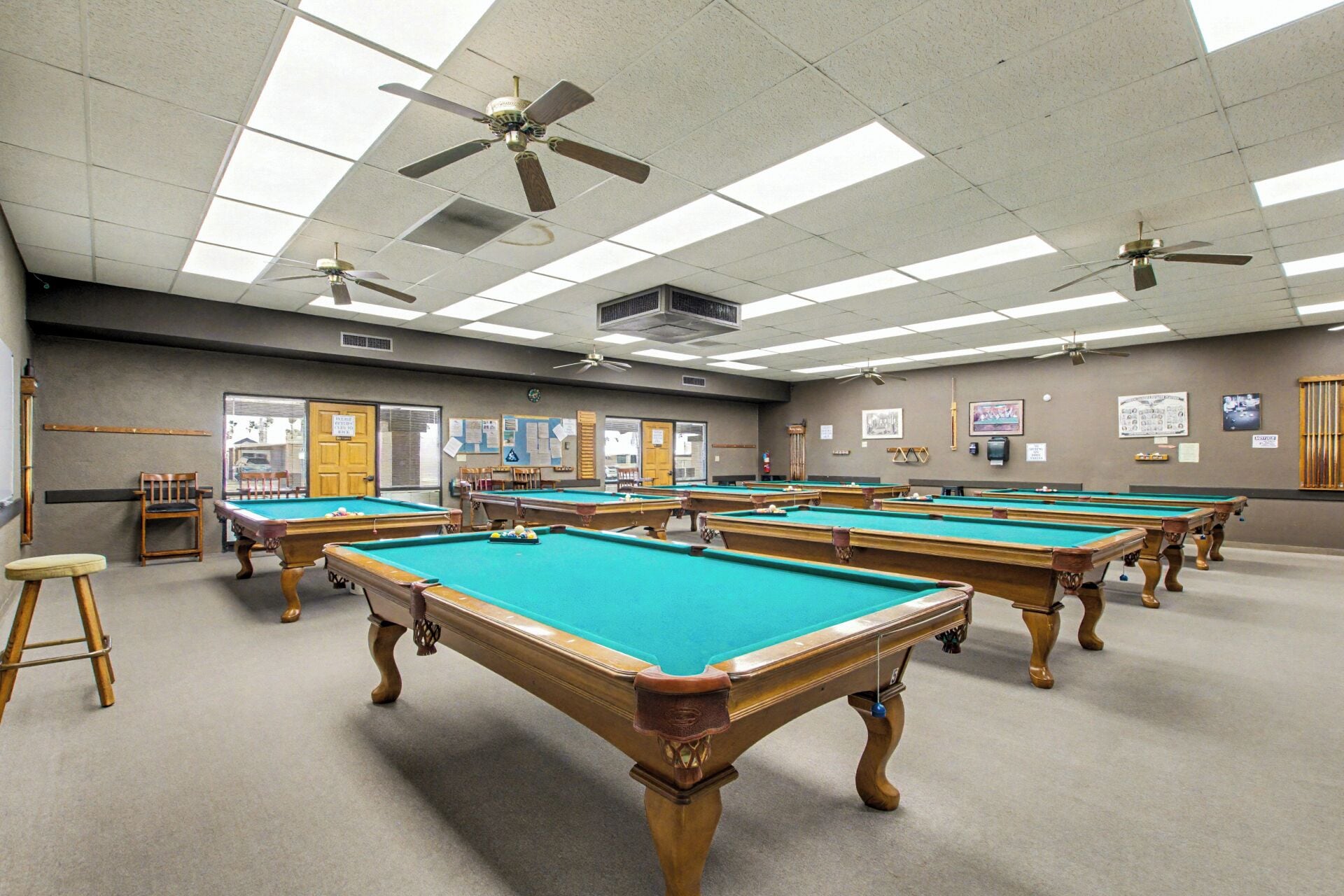 A pool hall with multiple pool tables, ceiling fans, and a bulletin board on the wall.