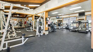 Un gimnasio con diversas máquinas de ejercicio, un espejo grande y una pantalla de televisión.