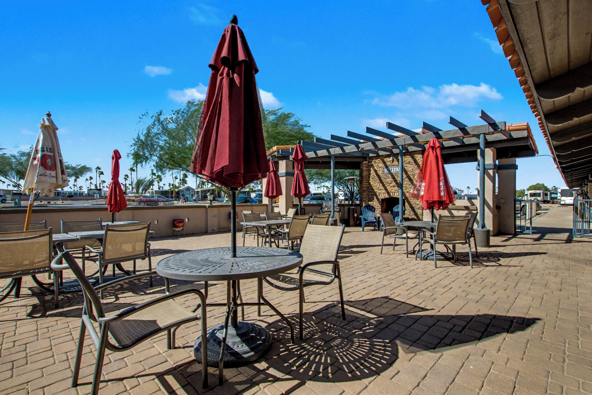 An outdoor patio area with round tables and chairs, red umbrellas, and a stone wall.