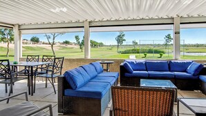 Un espacio al aire libre techado con sofás y sillones azules, una mesita y vista a un campo de golf.