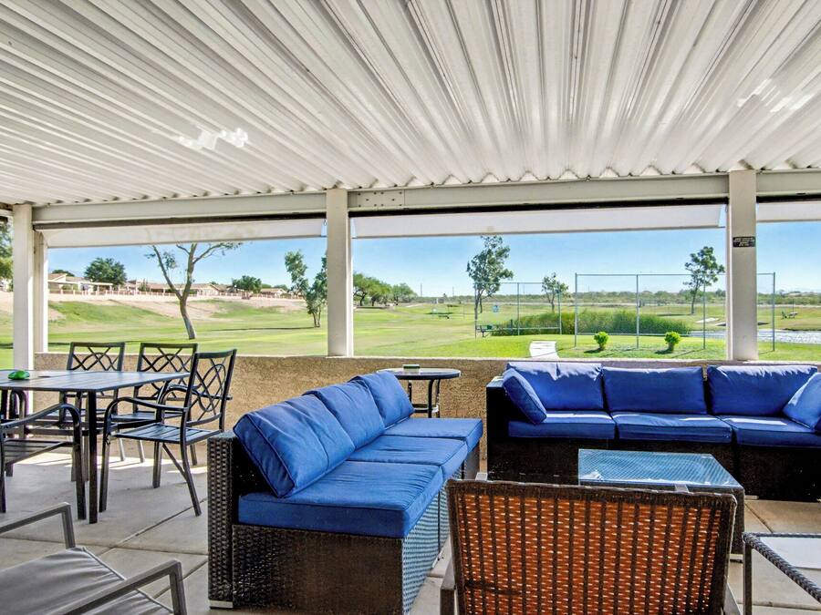 A covered outdoor seating area with blue sofas and chairs, a small table, and a view of a golf course.