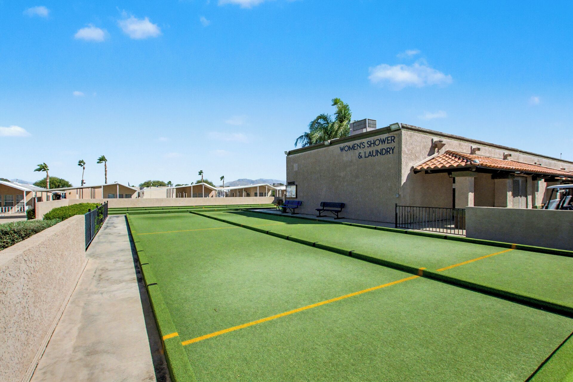 A women's showery and lounge area with a green turf sports court, palm trees, and a clear blue sky.