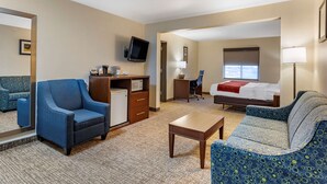 A hotel room with a blue armchair, a sofa, a bed, a desk, a television, and a window. - Comfort Inn & Suites Greenville I-70 (Greenville)