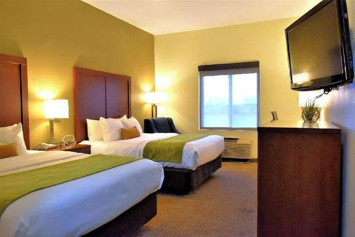 Ein Hotelzimmer mit zwei Betten, einem Fernseher, einem Fenster und einem Schreibtisch.