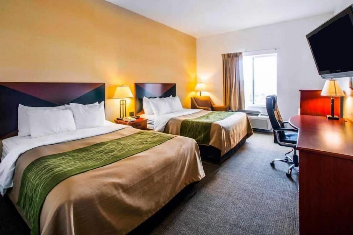 Ein Hotelzimmer mit zwei Betten, einem Schreibtisch, einem Stuhl, einem Fernseher und einem Fenster.