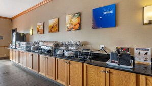 A hotel reception area with a long wooden counter, coffee machines, and a wall with framed pictures. - Comfort Inn & Suites Greenville I-70 (Greenville)