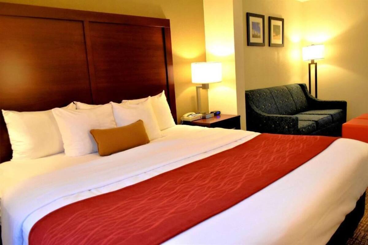 Ein Hotelzimmer mit einem großen Bett, einem Holzkopfteil, einem Schreibtisch mit Lampe und einem Sessel.