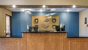 A reception desk with a wooden panel design, a large 'C' logo, and a glass partition. - Comfort Inn & Suites Greenville I-70 (Greenville)