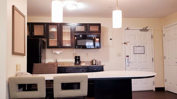 A compact kitchen with dark cabinets, a microwave, a coffee maker, and a white countertop. There are two wicker chairs and a small table.
