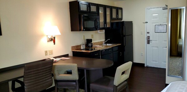 A compact hotel room with a kitchenette, a dining area with two chairs, a table, and a single lamp. - Candlewood Suites Houston Medical Center by IHG (Houston)