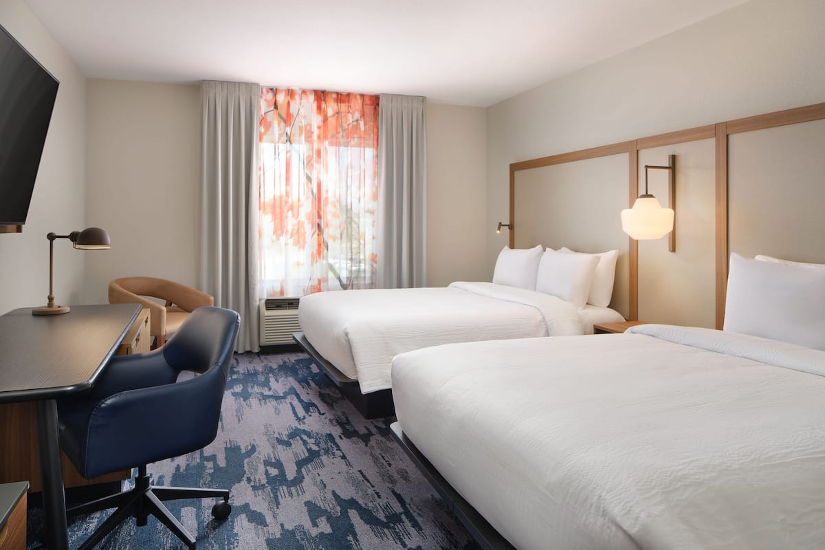A hotel room with two beds, a desk, a chair, and a TV.