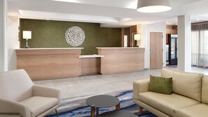 A modern hotel lobby with a reception desk, a sofa, a chair, and a coffee table.