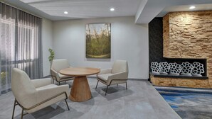 A modern living room with a round wooden table, two armchairs, and a stone fireplace.